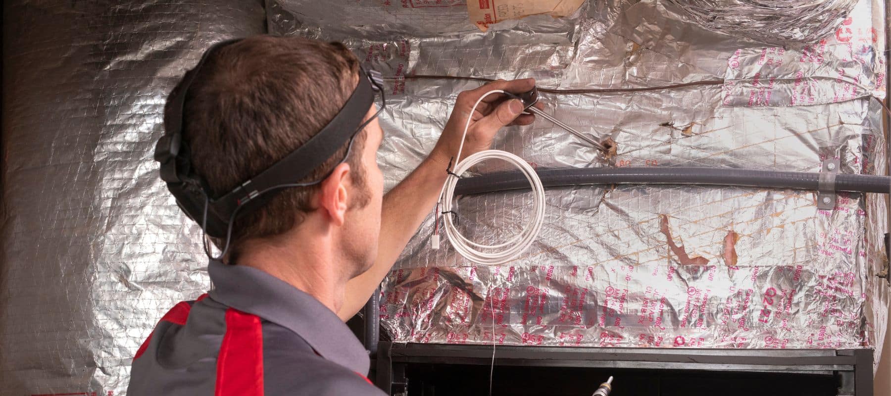 Technician working on ductwork wrapped in reflective insulation for HVAC maintenance