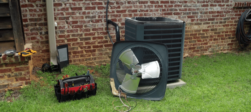 Air conditioning unit components, including a fan and toolbox, set up outside a brick wall