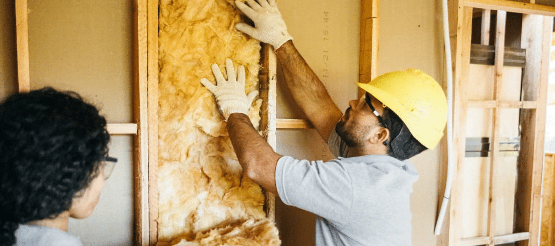 A worker installing fiberglass insulation in a residential wall for energy efficiency