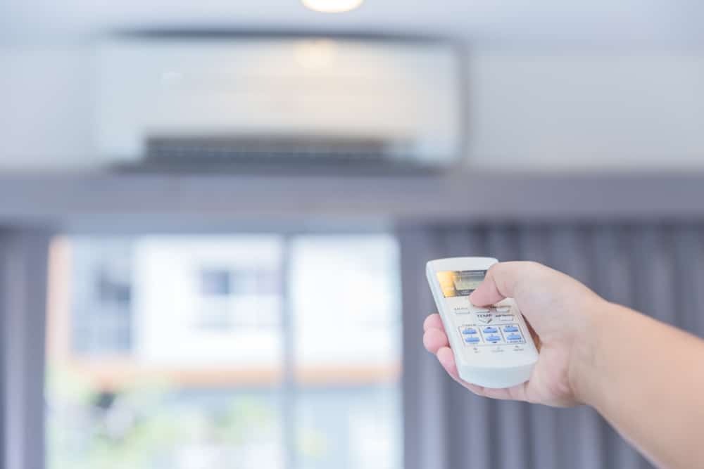 hand holding white remote pointing at a ductless air handler in a home