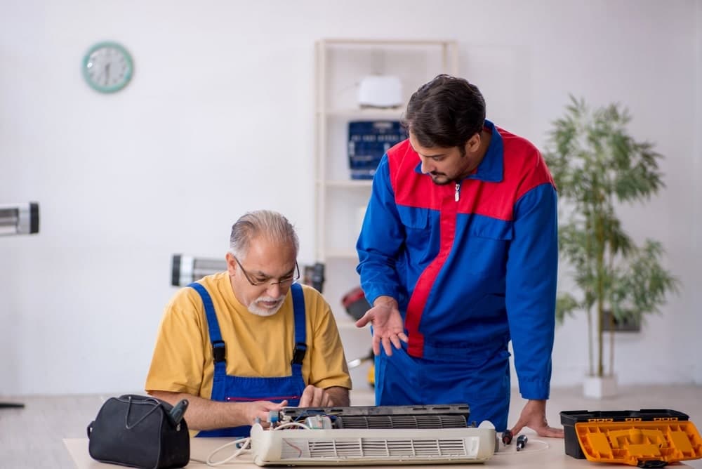 AC technician leaning over homeowner sitting at table explaining AC issue